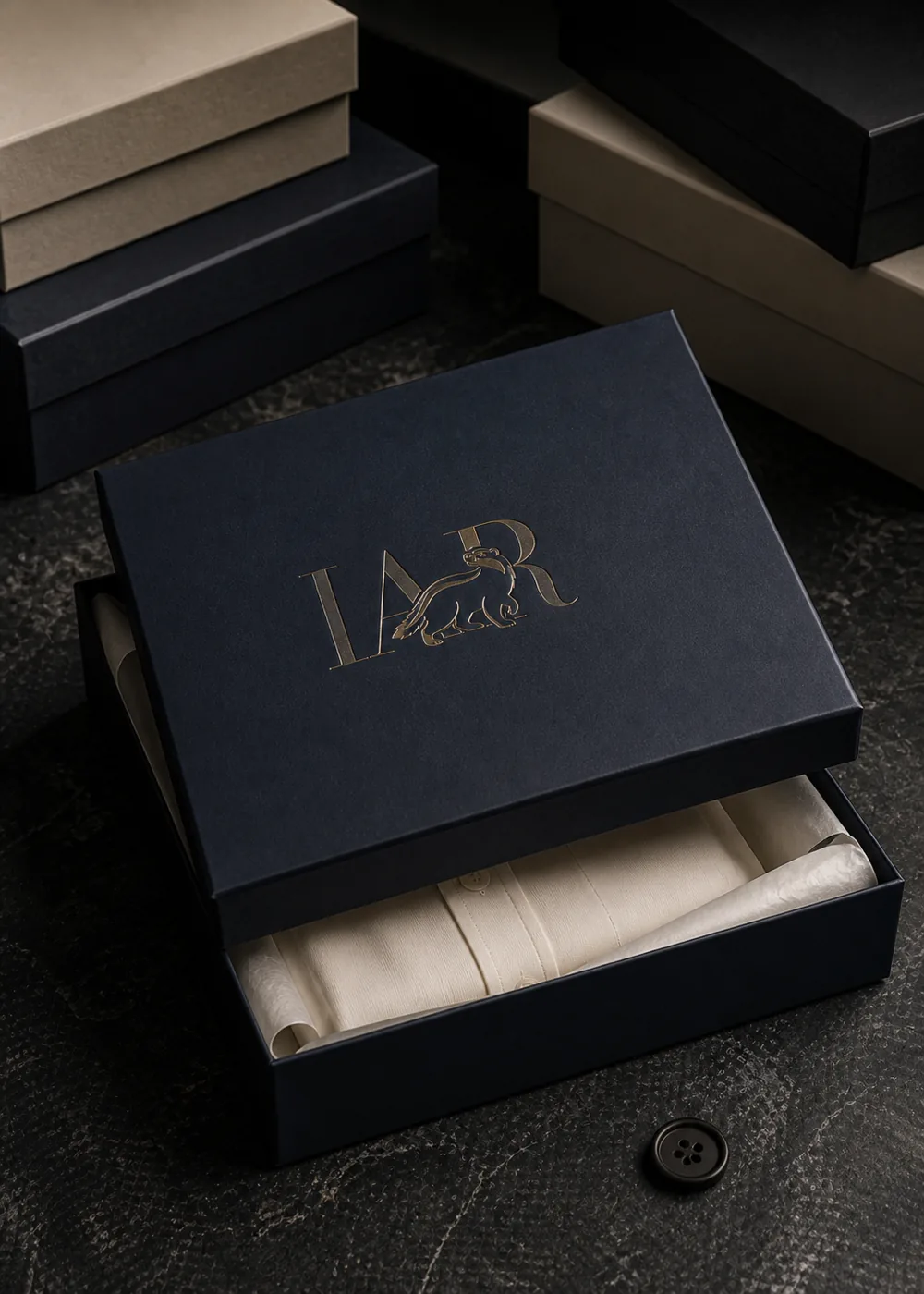 The house box in navy, the I Am Ratan mark foiled across the lid, the
             lid lifted to show tissue and a folded shirt inside