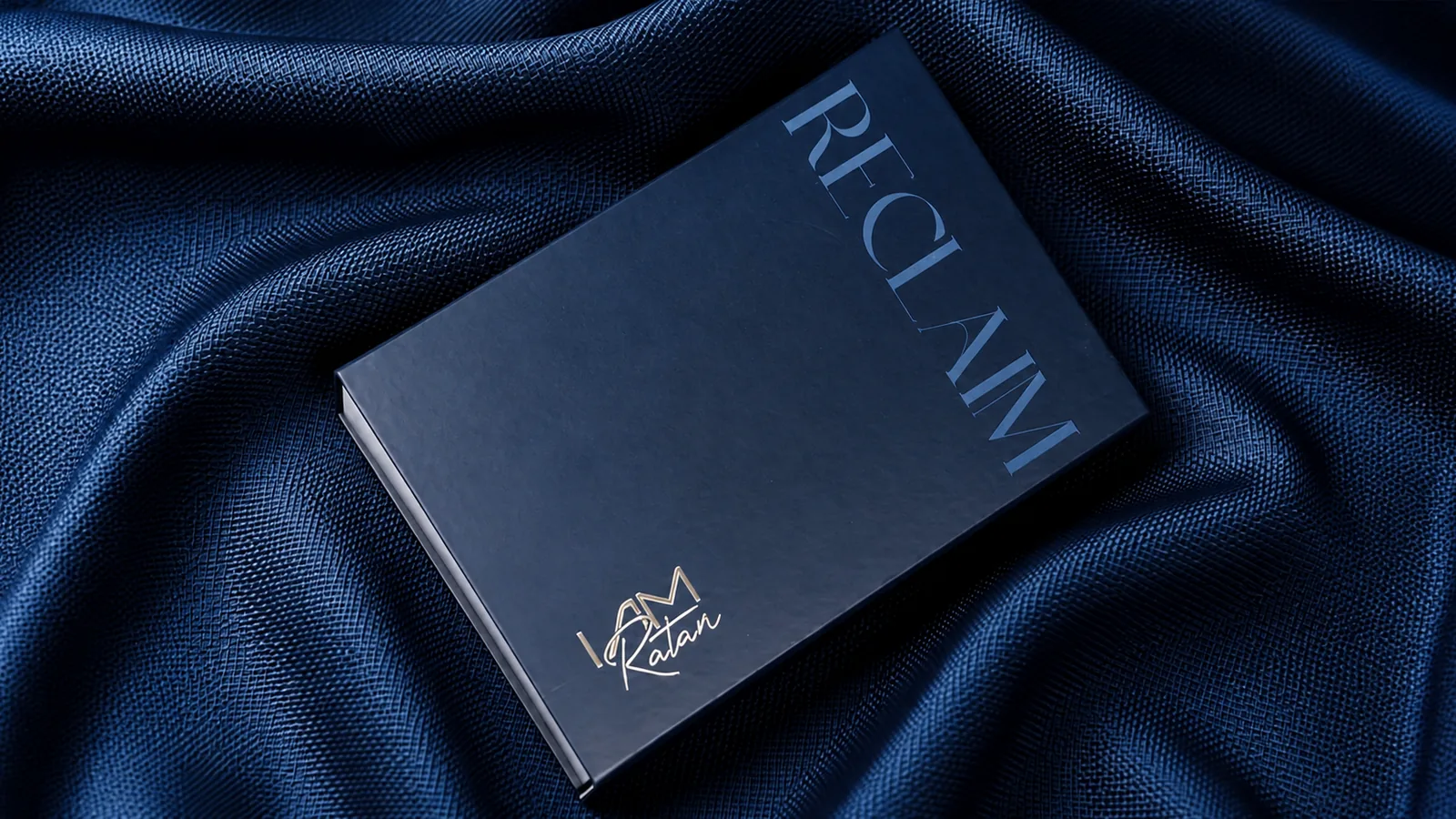 The house box in navy, RECLAIM foiled across it and the I Am Ratan signature below, on blue cloth